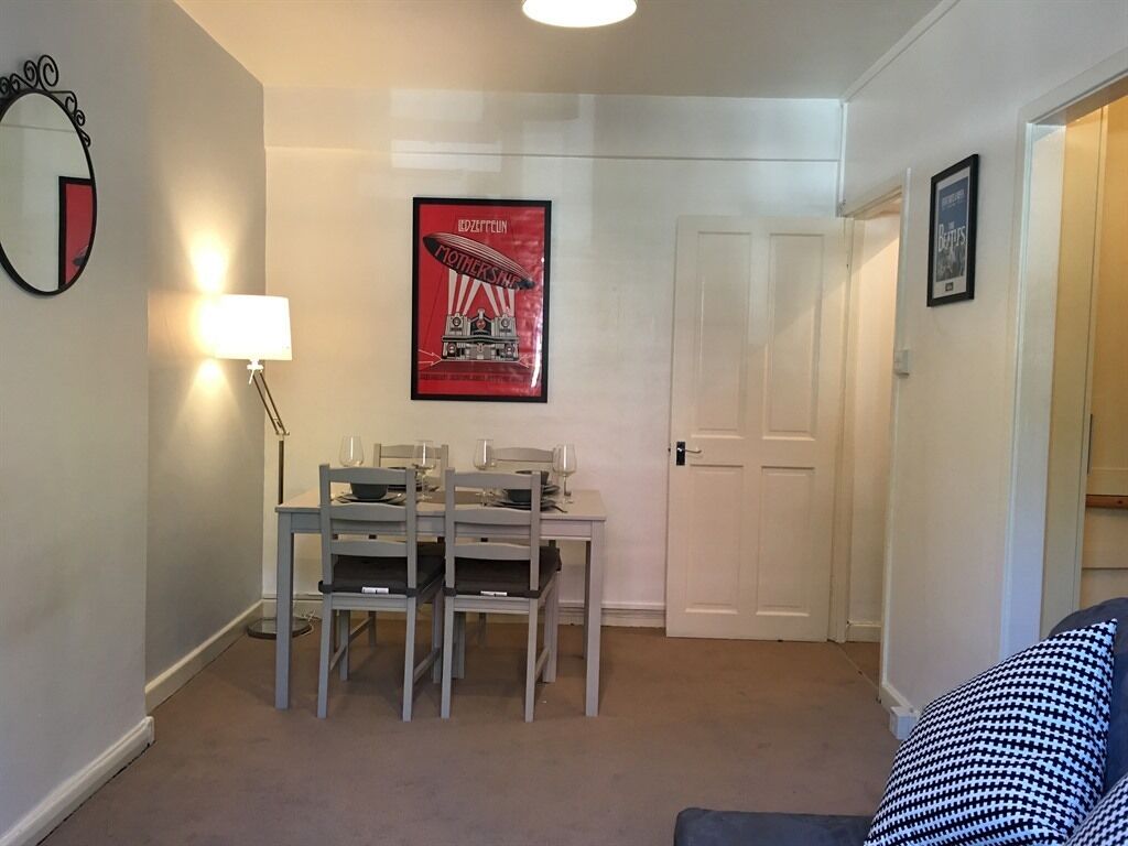 A dining area with a table and chairs, a lamp, and a framed poster on the wall.