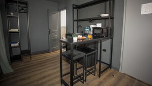 Una cocina compacta con microondas integrado, un pequeño comedor con taburetes y una estantería metálica.