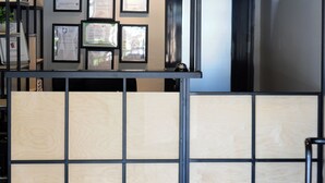 Un área de recepción con un separador de madera, certificados enmarcados en la pared y una escalera de metal.