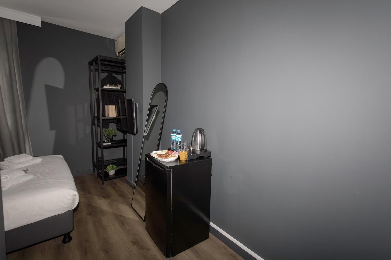 A hotel room with a bed, a small desk with a kettle, a water bottle, and a juice bottle.