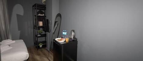 Una habitación de hotel con una cama, un pequeño escritorio con hervidor, una botella de agua y una botella de jugo.