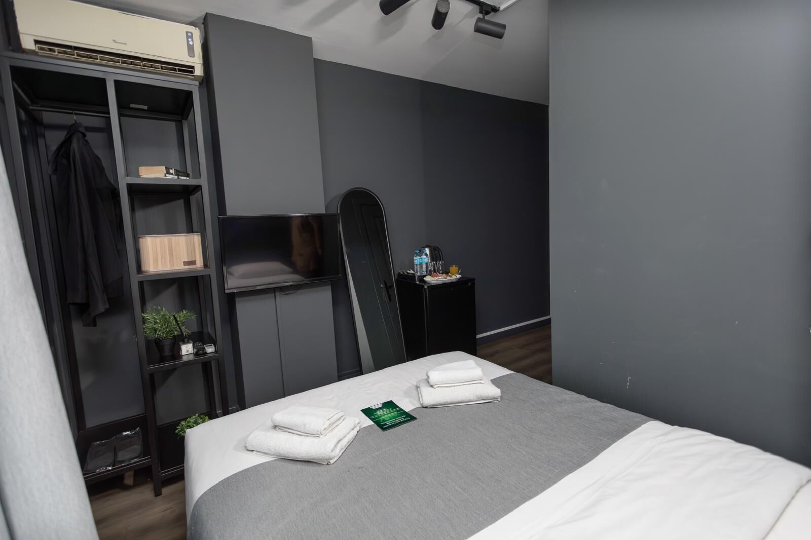 A hotel room with a bed, a wardrobe, a TV, and a small table with a kettle and water bottle.