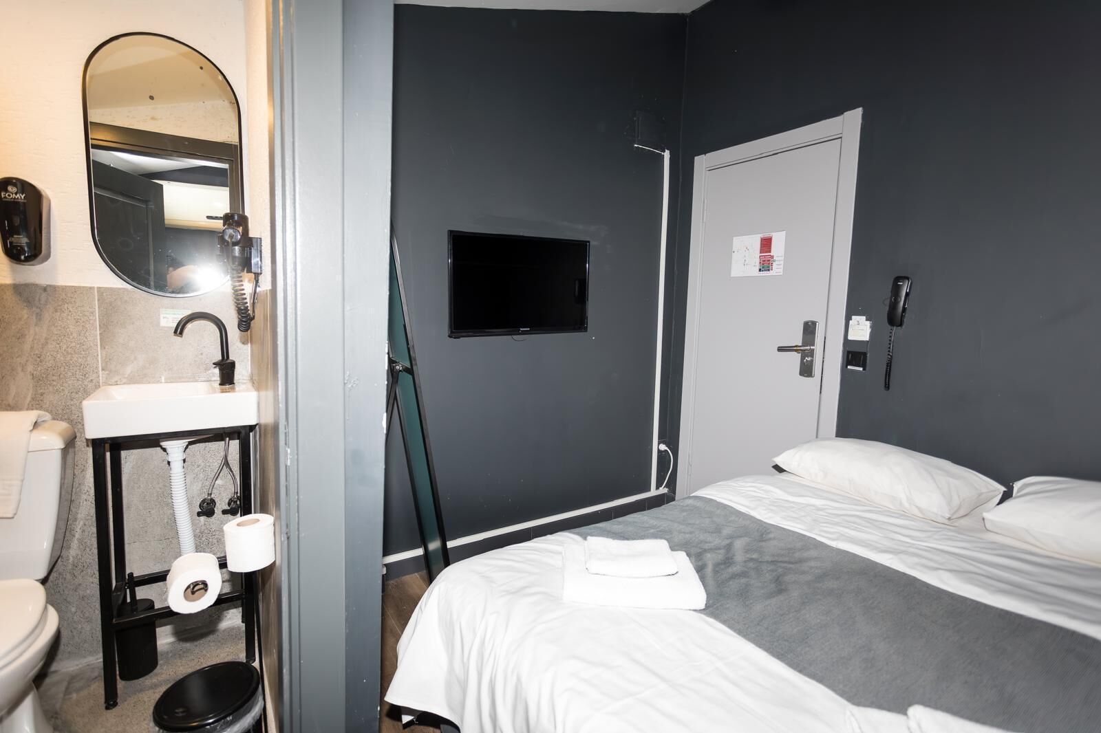 A hotel room with a bed, a small bathroom with a sink, toilet, and a mirror.