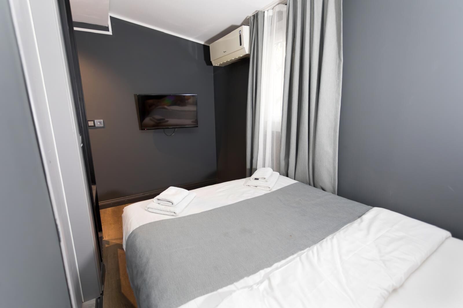Habitación de hotel con cama, televisor de pantalla plana montado en la pared y ventana con cortinas.