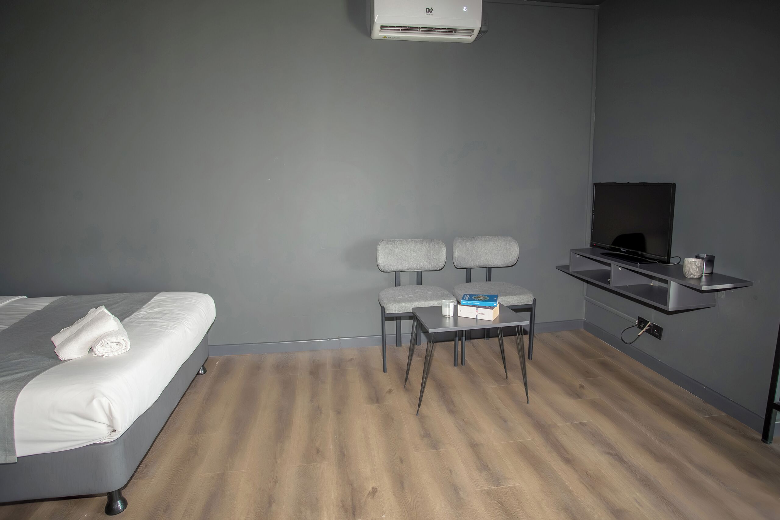 Una habitación de hotel con cama, escritorio, dos sillas, televisor y una pequeña estantería.