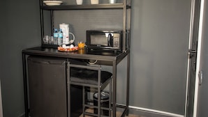 Una kitchenette compacta con microondas, refrigerador pequeño y estante con plantas en macetas.
