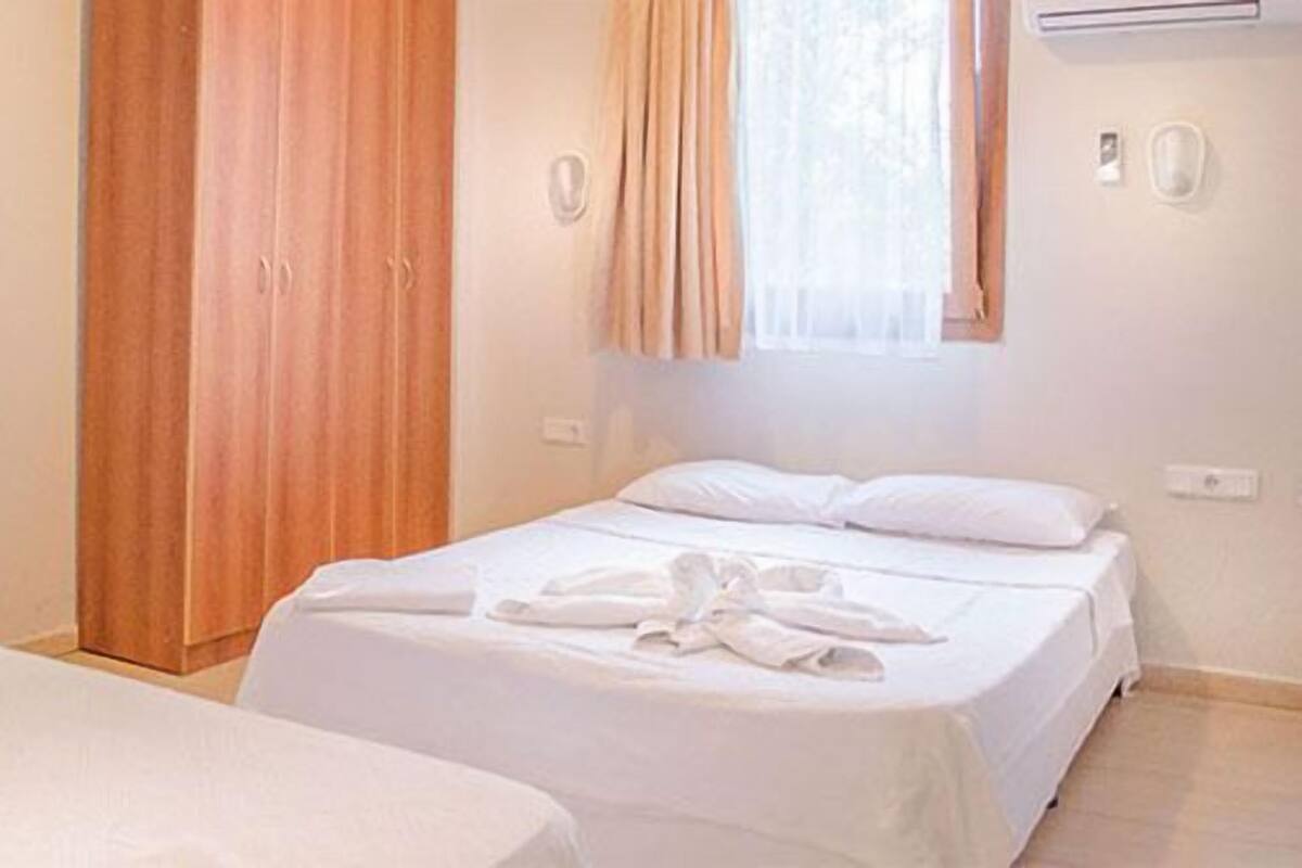 Habitación de hotel con dos camas, un armario de madera, una ventana con cortinas y un equipo de aire acondicionado.