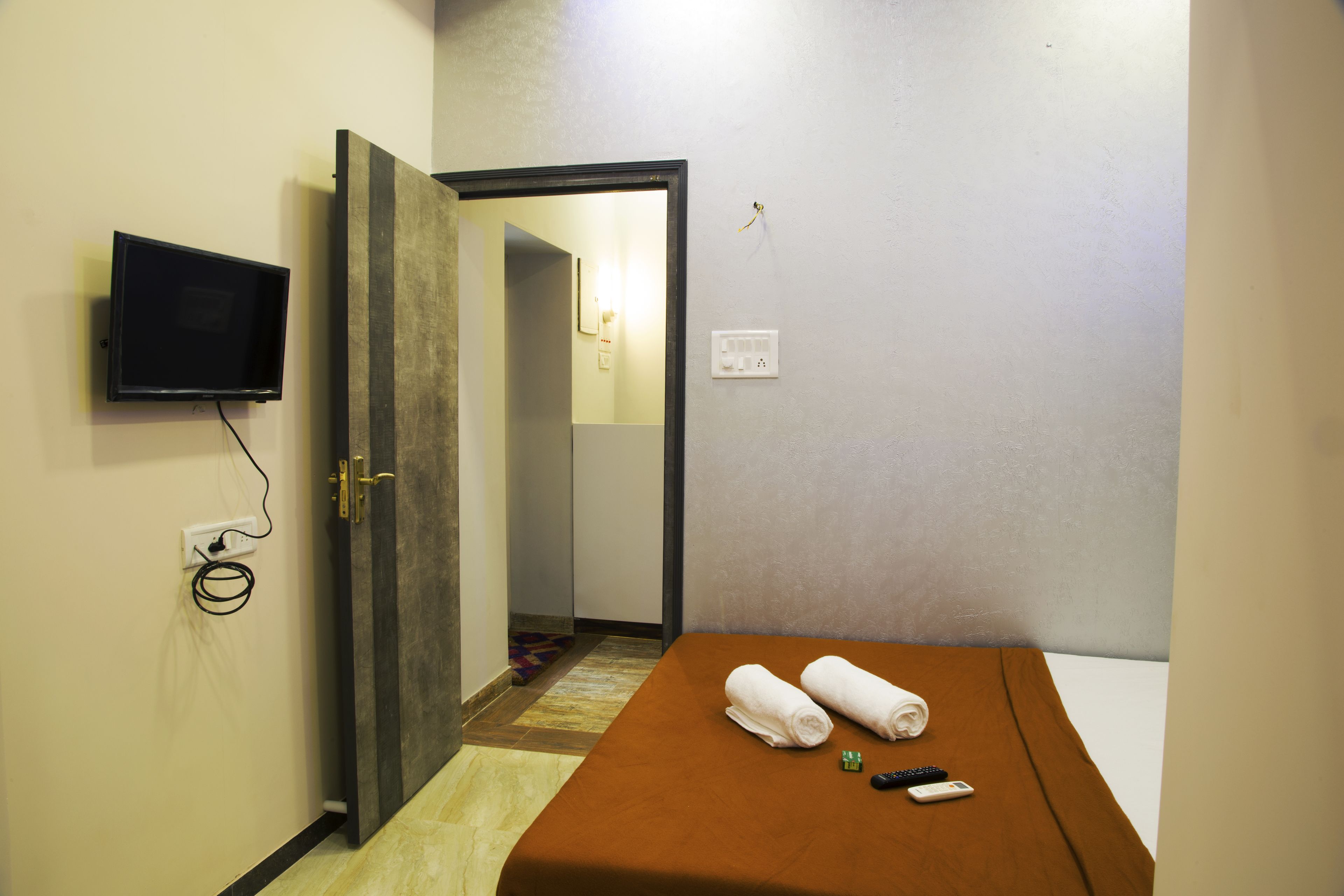 Una habitación de hotel con una cama, un televisor fijado a la pared y una puerta que da a otra estancia.