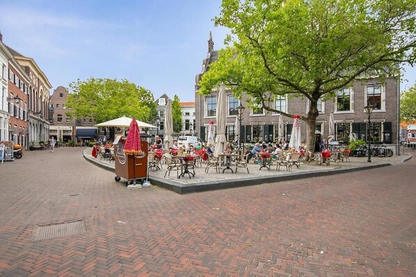 A cobblestone square with outdoor seating, a central kiosk, and historic buildings in the background.