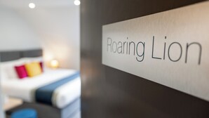 A hotel room with a bed, a nightstand, and a sign that reads "Roaring Lion." - Stableside at York Racecourse (York)