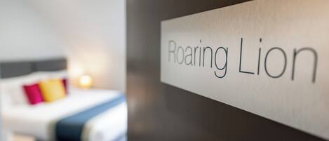A hotel room with a bed, a nightstand, and a sign that reads "Roaring Lion."