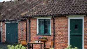 A brick building with a tiled roof, a green door, and a window with a flower box. - Stableside at York Racecourse (York)