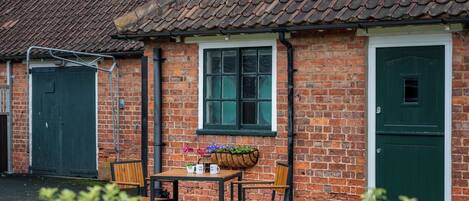 A brick building with a tiled roof, a green door, and a window with a flower box.