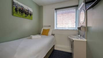 Une petite pièce propre, avec un lit simple, une fenêtre avec des stores, un radiateur et un lavabo.