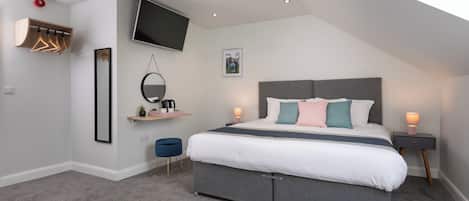 A modern bedroom with a large bed, a TV mounted on the wall, a small desk, and a ceiling light.