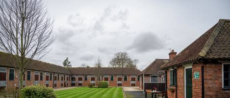 A courtyard with a lawn, brick buildings, and a small seating area with a table and chairs.