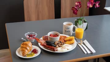 Une table de petit-déjeuner avec des assiettes remplies de nourriture, une tasse de café, un verre de jus d’orange et une fleur.