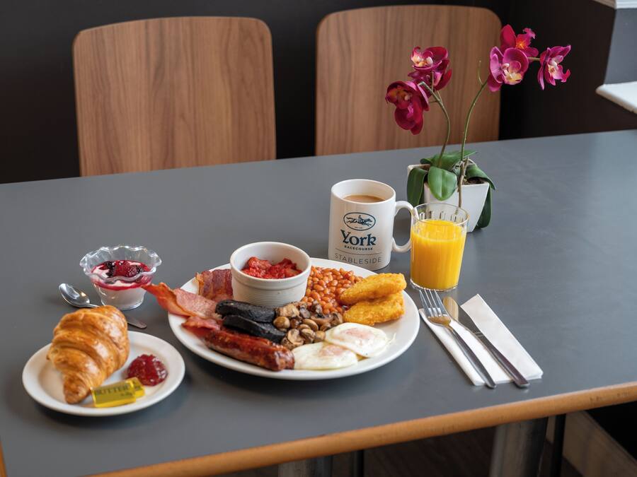Une table de petit-déjeuner avec des assiettes remplies de nourriture, une tasse de café, un verre de jus d’orange et une fleur.