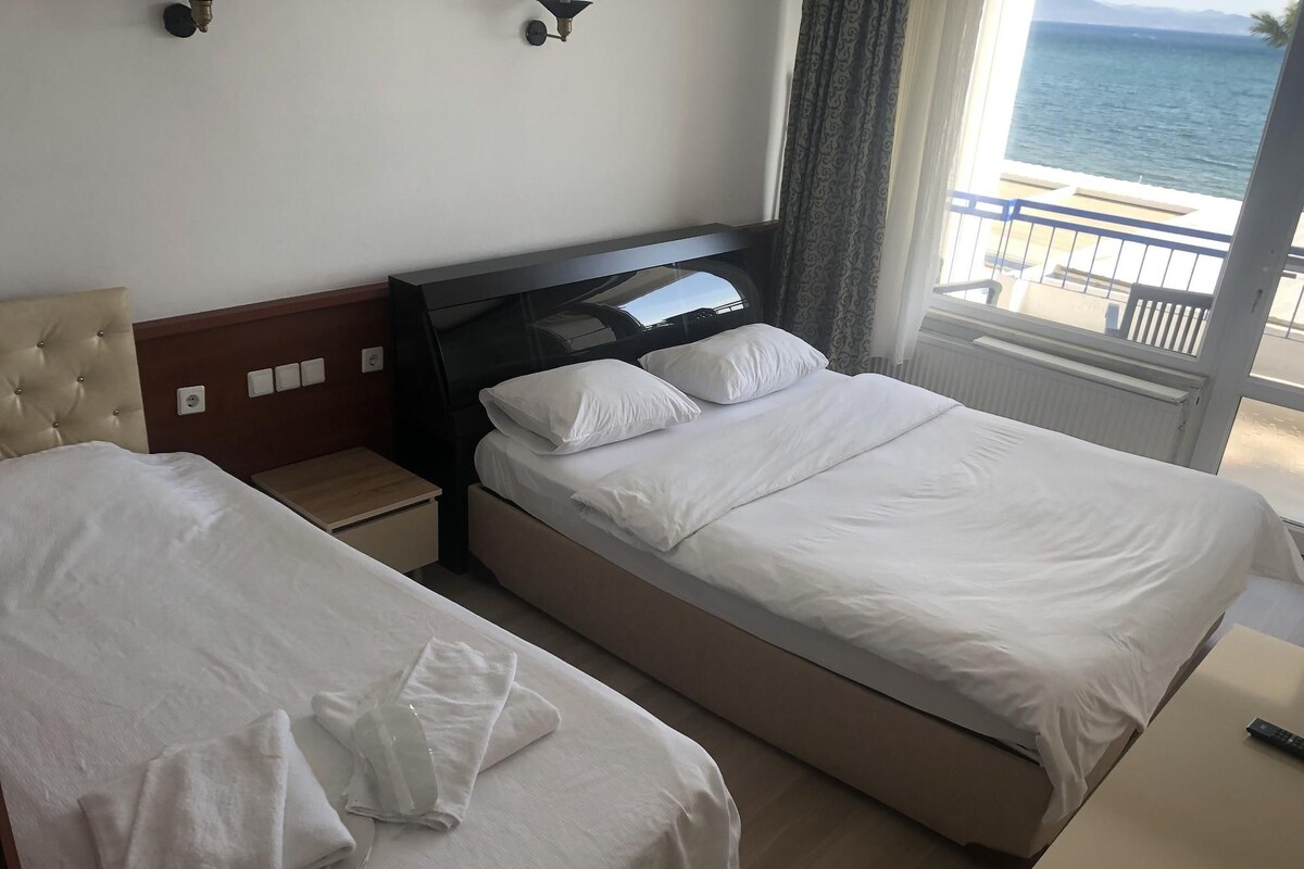 Ein Hotelzimmer mit zwei Betten, einem Nachttisch, einer Wandlampe und Meerblick.