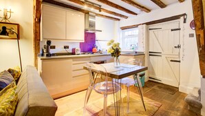 A modern kitchen with wooden beams, a dining table with chairs, and a vase of flowers. - Cartref (Farnham)