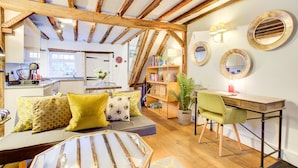 A cozy living room with a wooden ceiling, a sofa with yellow cushions, a glass coffee table, and a desk with a chair. - Cartref (Farnham)