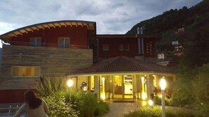 Un hotel con fachada de piedra, un acceso cubierto y vistas a las colinas circundantes.