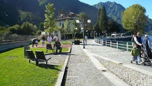 Un sendero pavimentado con bancos, un lago y montañas al fondo.