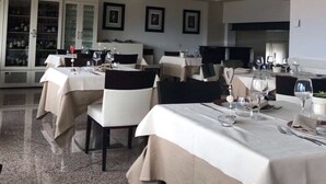 Un restaurante con varias mesas dispuestas para comer, una lámpara de araña grande y una bodega en el fondo.