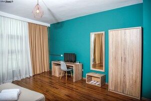 Una habitación con un escritorio de madera, una silla, una cama, un armario y un espejo.