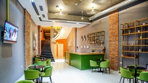 Un interior moderno con un mostrador de recepción, sillas verdes y una escalera que lleva a un nivel superior.