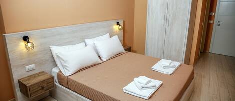 A neatly made bed with white linens and a brown bedspread, a wooden nightstand with a drawer, and a wardrobe with a light wood finish.