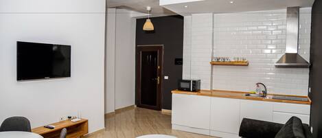 A modern kitchen with white cabinets, a wooden countertop, and a built-in microwave. There is a dining area with a round table and chairs, and a black sofa.