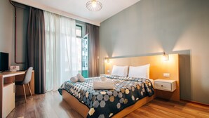 Una habitación de hotel con cama, escritorio, silla, mesita de noche y ventana con cortinas.