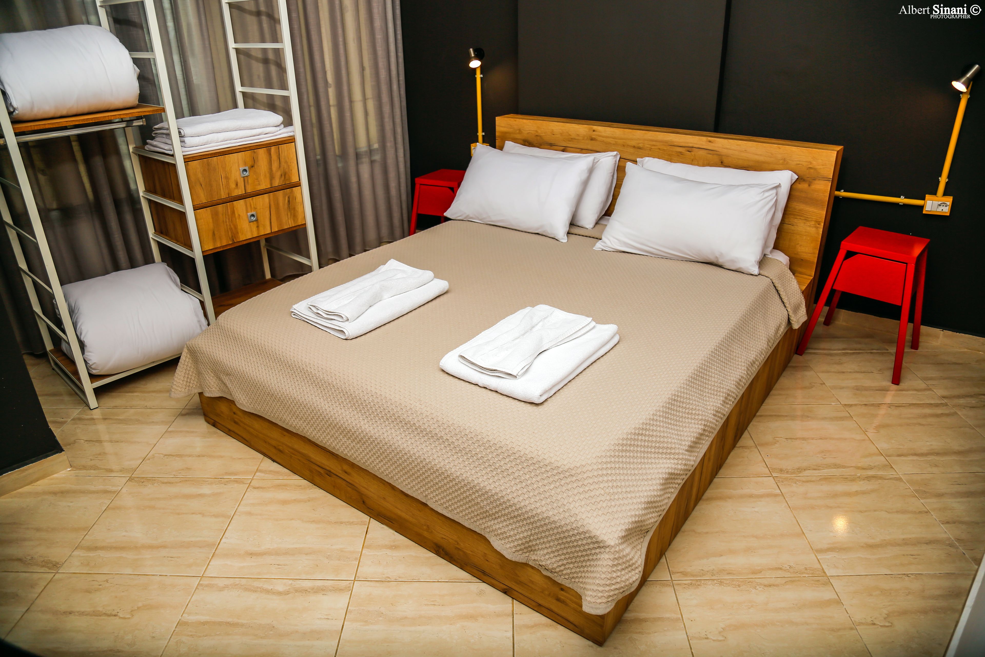 A neatly made bed with white linens, a wooden headboard, and a red nightstand with a lamp.
