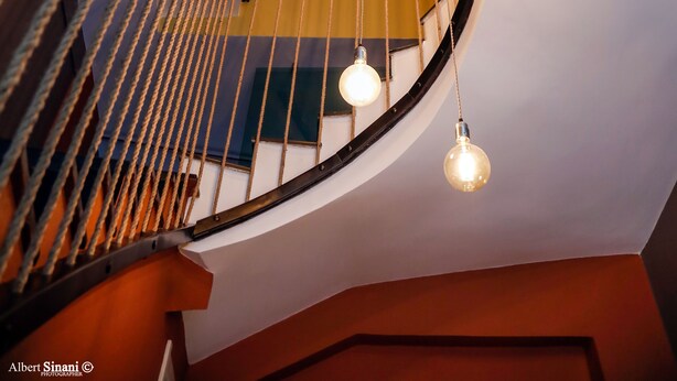 Una escalera de caracol con un diseño moderno, que incluye una barandilla de madera y varios focos colgantes.