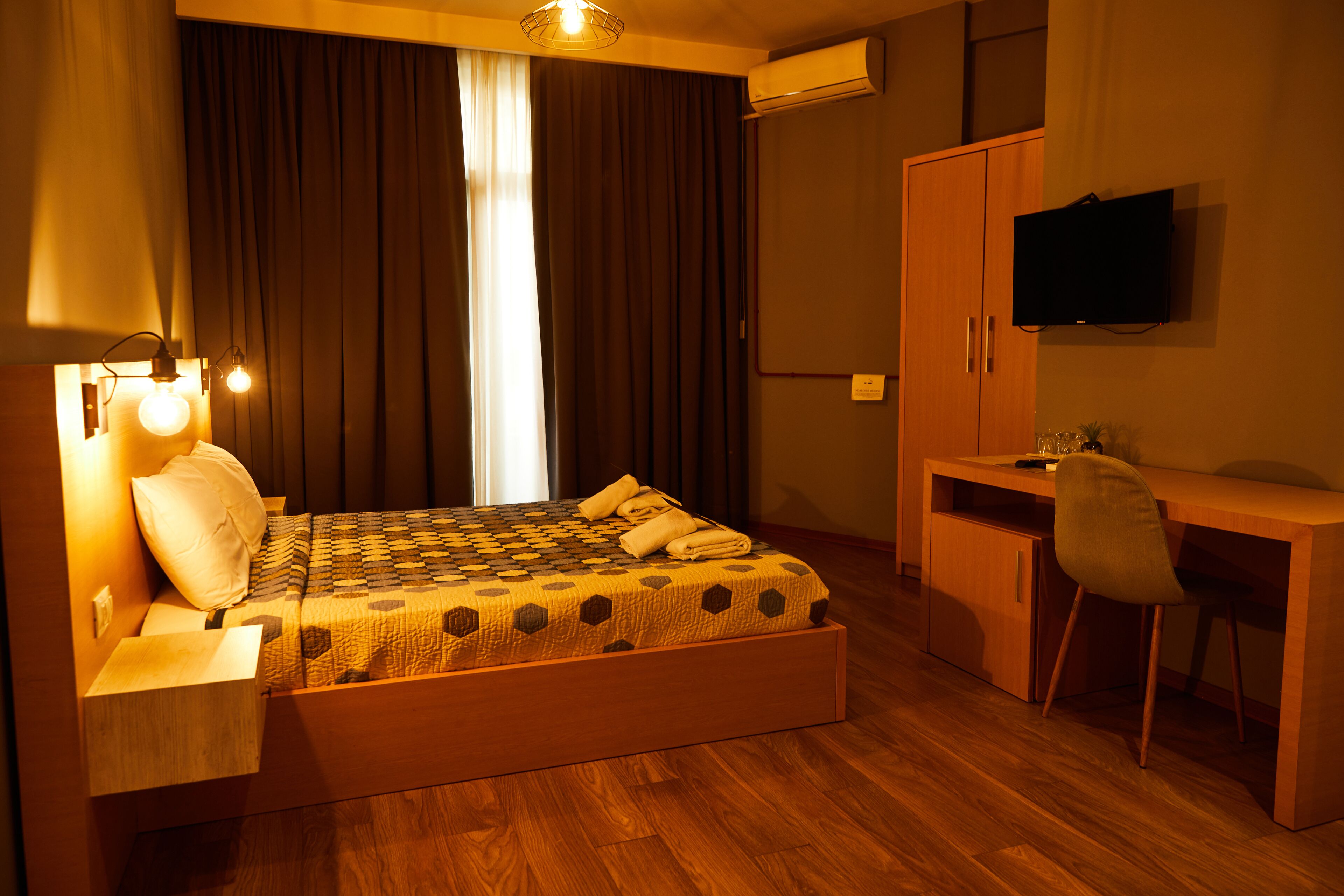 A bedroom with a bed, bedside table, desk, chair, and a television.