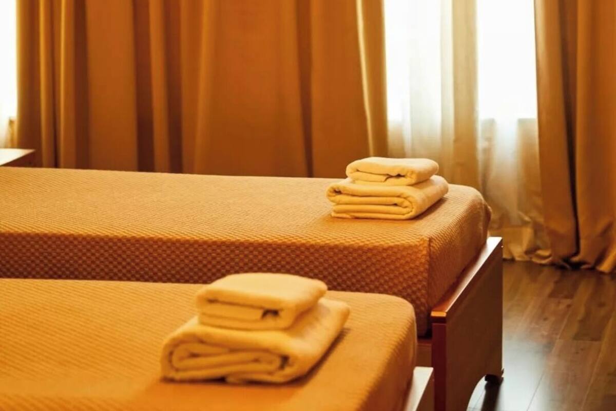 Two beds with folded towels, a wooden floor, and a window with curtains.