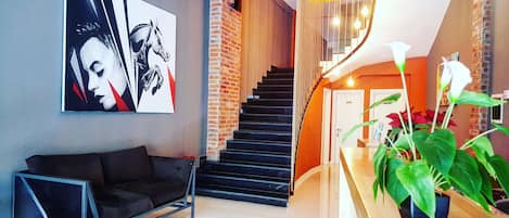 Un salon moderne avec un canapé noir, une grande peinture abstraite, un escalier et une plante en pot.