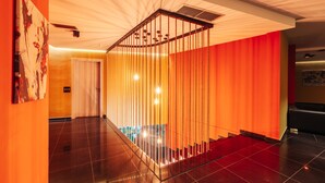 Un moderno vest íbulo de hotel con una escalera, una recepción y un cuadro abstracto grande en la pared.