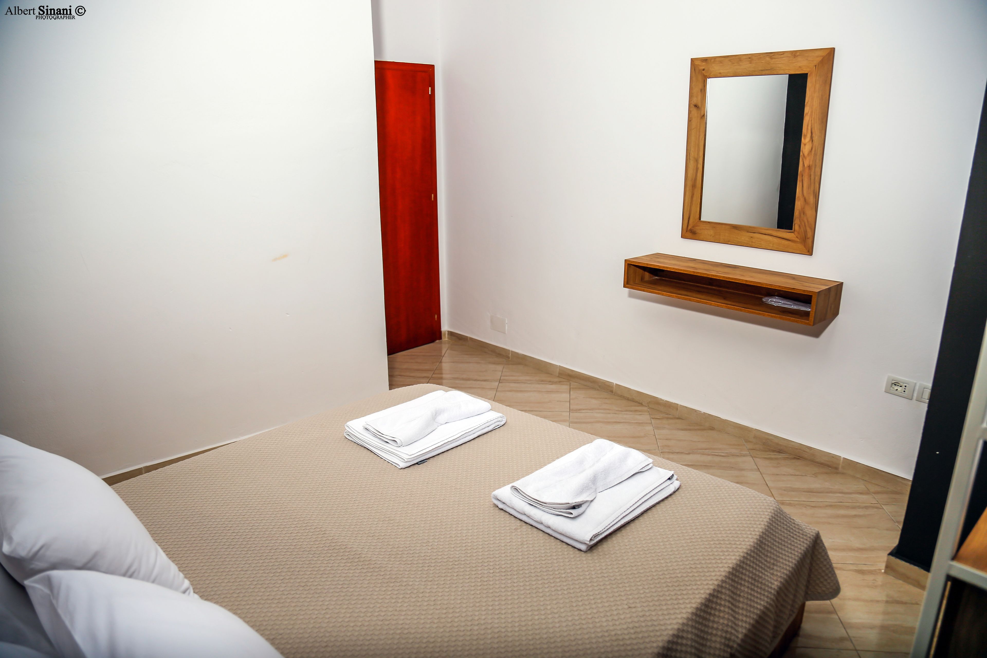 Una habitación de hotel con una cama, un estante de madera y un espejo en la pared.