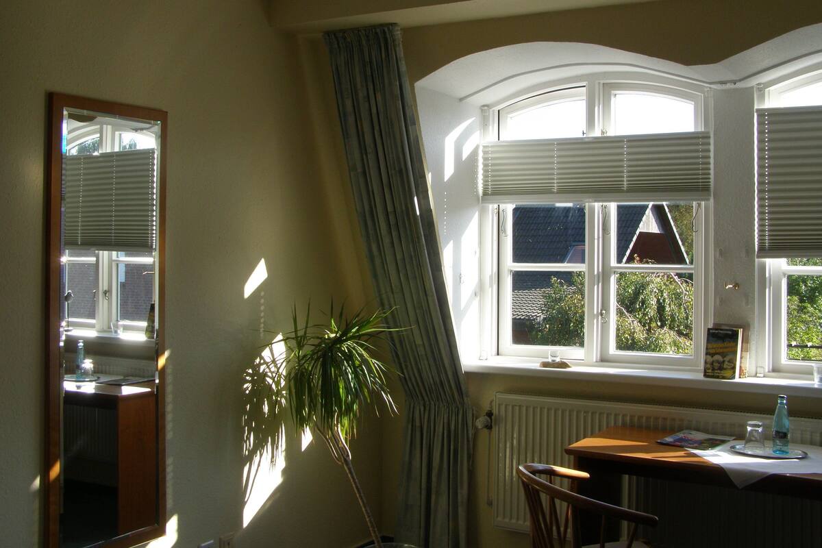 A room with a large window, a radiator, a table with a bottle, and a plant.