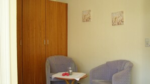 A room with a wooden wardrobe, two armchairs, a small table with a glass and a red object, and two wall-mounted floral paintings. - Faehrhaus Niederkleveez (Bösdorf)