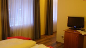 A hotel room with a bed, a television on a wooden cabinet, and a window with curtains. - Faehrhaus Niederkleveez (Bösdorf)