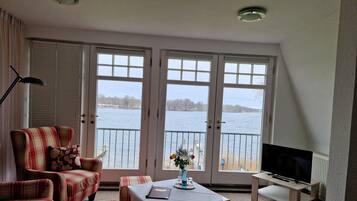 Une pièce avec vue sur un lac, comprenant un canapé à carreaux, une petite table avec un vase et un téléviseur posé sur un meuble.