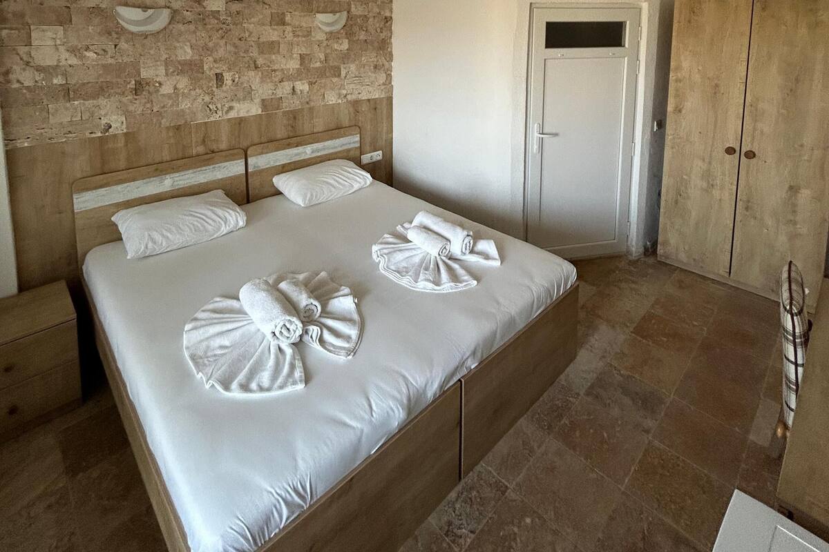 A hotel room with a large bed, a wooden headboard, a ceiling fan, and a wardrobe.