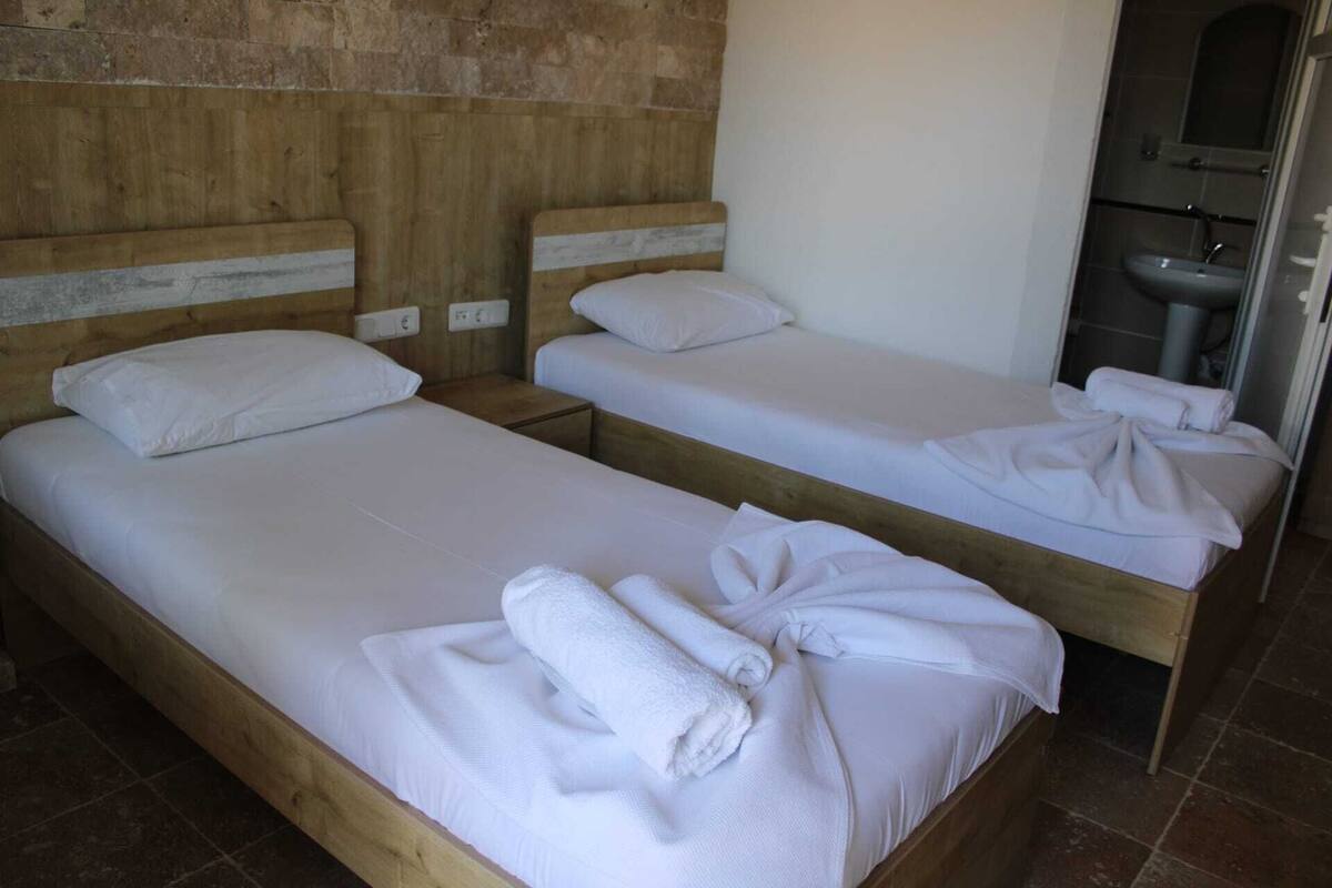 A room with two wooden beds, each with white linens and pillows, and a small bedside table.
