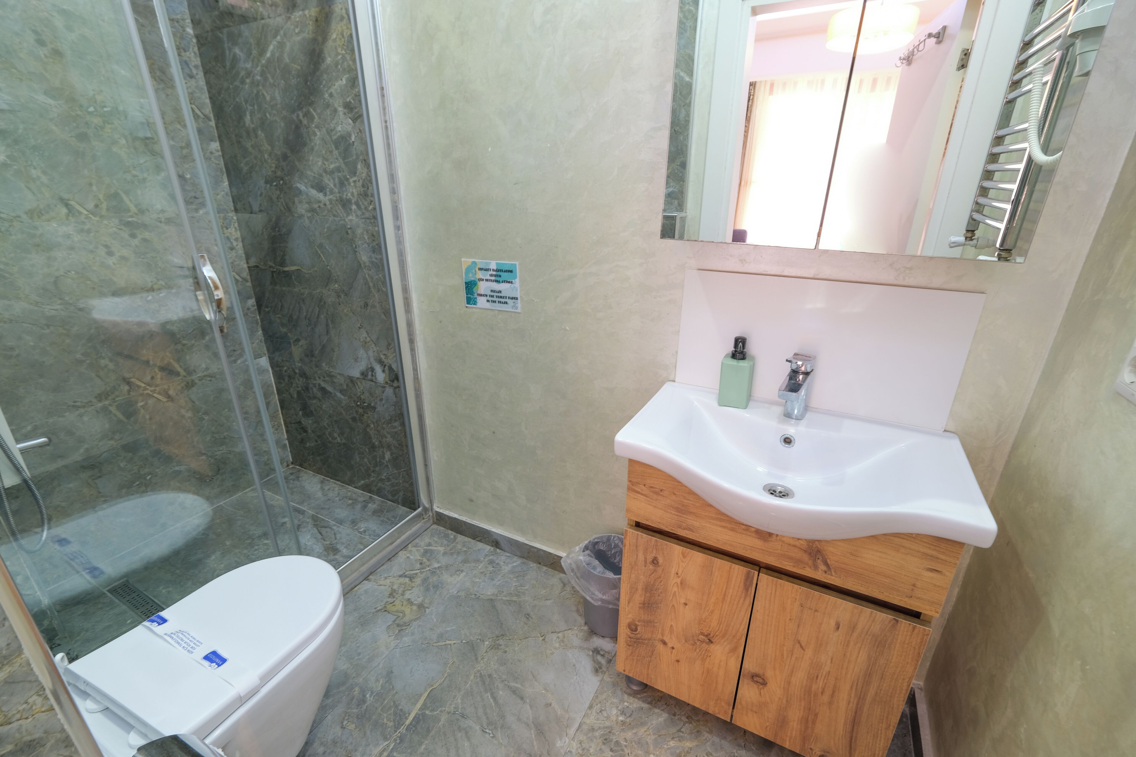 A bathroom with a glass-enclosed shower, a white toilet, a wooden cabinet with a sink, and a mirror above the sink.