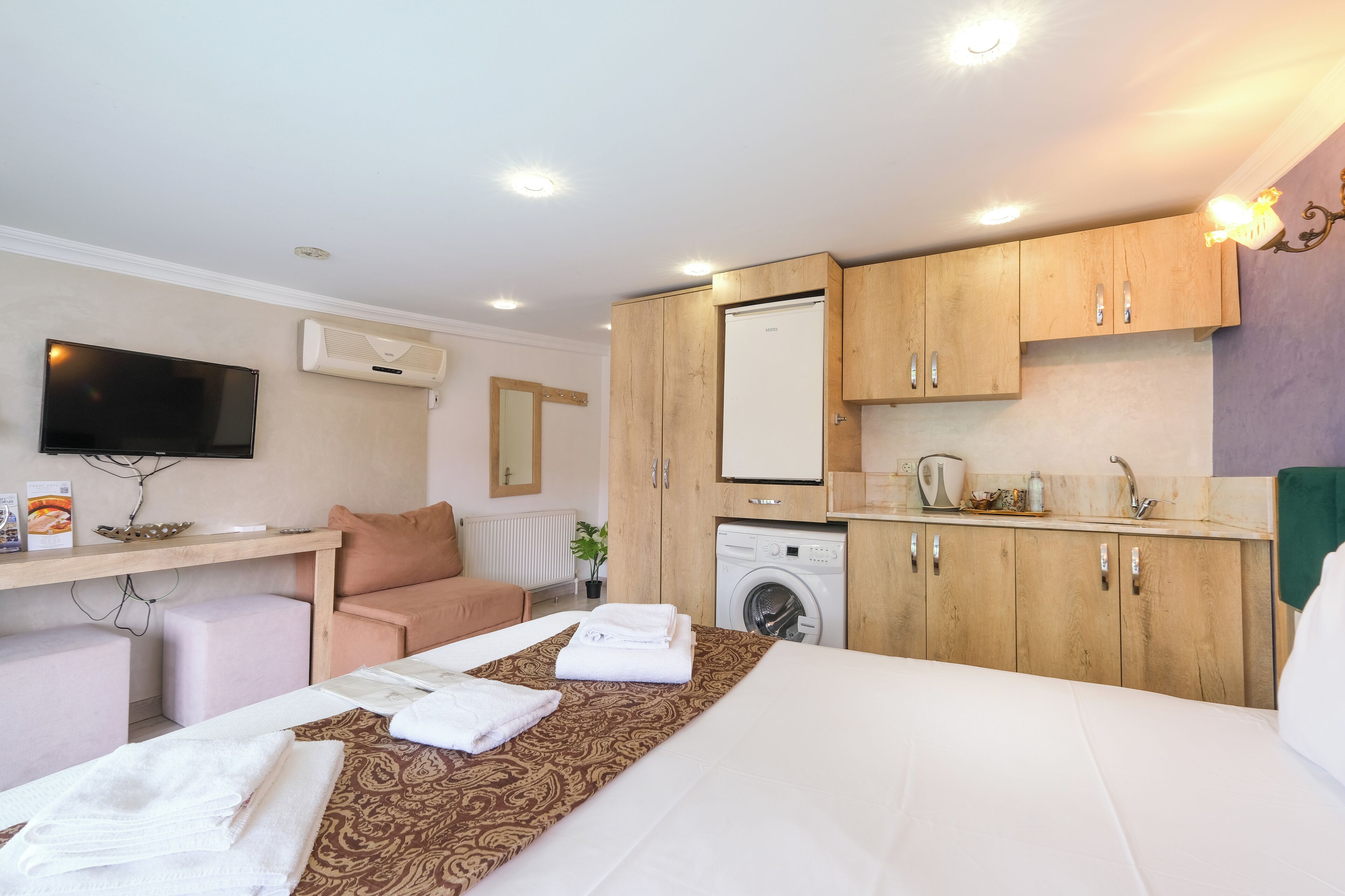 A hotel room with a bed, a washing machine, a sink, and a television.
