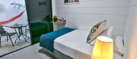 Un dormitorio con cama, lámpara de noche, mesita, silla y vistas al exterior.