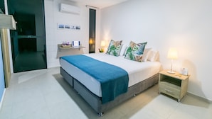 Una habitación de hotel moderna con una cama grande, una mesita de noche con lámpara y un escritorio pequeño con silla.